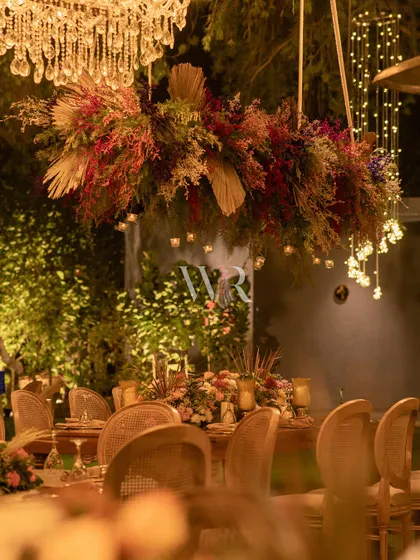 Another view of the boho dining area, showing the hanging floral chandelier and the warm, inviting tablescape. This design is perfect for a relaxed yet stylish day-to-night celebration.