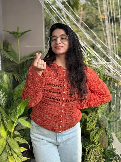This beautiful rust-colored cardigan features delicate openwork stitching and pearl-like buttons. It's a lightweight yet warm piece that can be dressed up or down, making it a versatile addition to your wardrobe.
