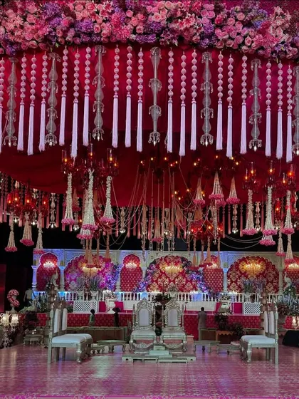 A magnificent, circular mandap structure with a canopy of red fabric and thousands of hanging floral tassels and crystals. This design creates a dramatic and opulent focal point in the center of the grand hall.