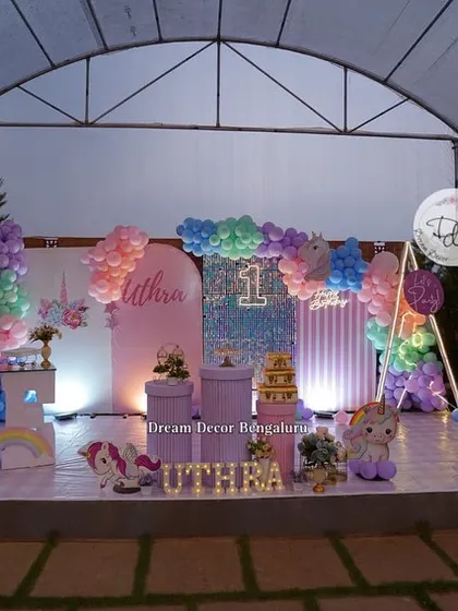 An outdoor unicorn-themed first birthday party. The setup features a large stage with pastel backdrops, a sequin wall, and of course, plenty of unicorns.