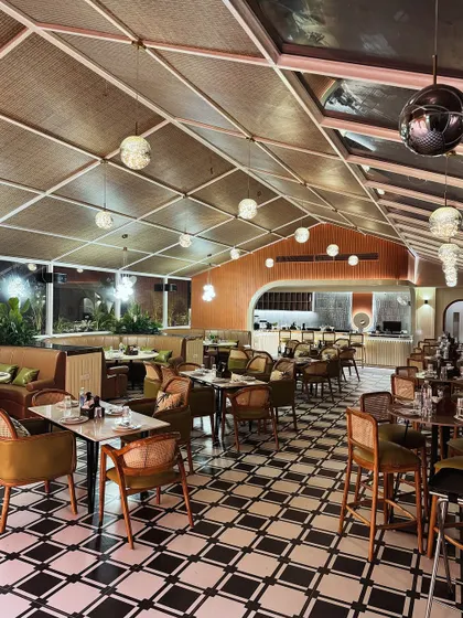 The main dining hall at Tipsy Town in Ayodhya, where classic and modern elements meet. The black-and-white checkered floor provides a bold graphic base, balanced by the warmth of tan leather seating and a woven ceiling texture.