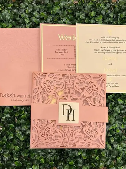 A modern laser-cut invitation in pastel pink. The intricate geometric pattern is complemented by a simple band with the couple's monogram.
