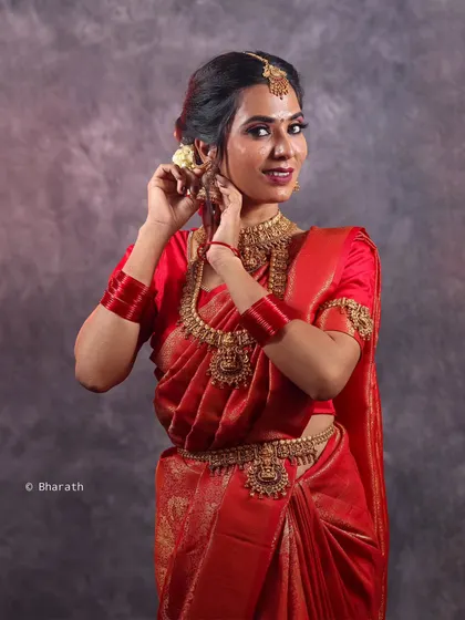 A close-up detail from a traditional saree shoot in the studio, focusing on the gesture of adjusting an earring, adding a natural touch to the posed shot.