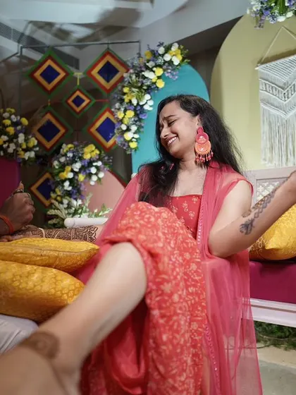 A candid moment of laughter during the Mehendi application. The colorful, modern backdrop with geometric patterns and floral details makes the moment even more special.