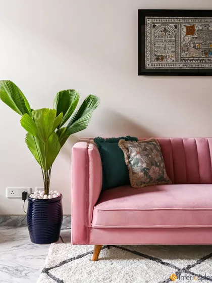 A detail shot of a pink velvet sofa, showing its channel-tufted back. The addition of a large plant and traditional artwork creates a beautiful contrast of styles.
