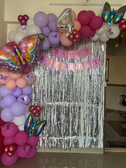 A fun butterfly theme for a 4th birthday, using a silver fringe curtain, a colorful balloon half-arch, and large butterfly foil balloons.