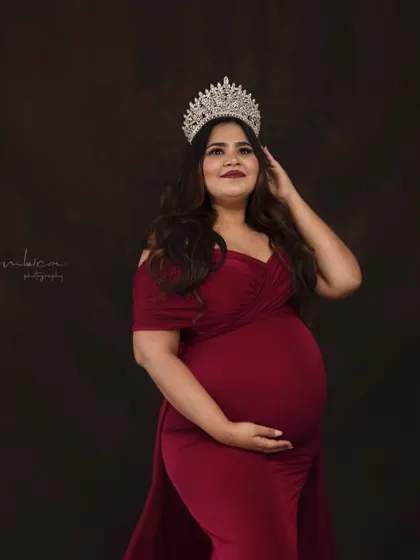 A classic portrait from the "Queen" session, focusing on her radiant and confident expression. The rich red gown and sparkling crown make for a powerful and glamorous maternity look.