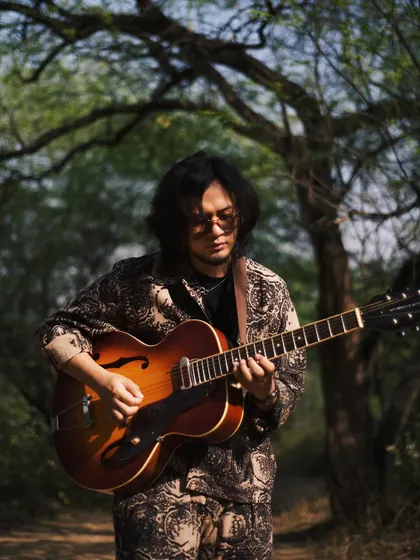 Taba Chake with his guitar in a forest clearing. This image connects the artist to nature, the source of so much inspiration.