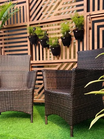 A cozy balcony in Gurugram featuring comfortable wicker chairs on a bed of artificial grass. The wooden screen adds privacy and a decorative backdrop.
