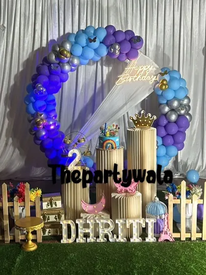 A blue and purple balloon ring with a 'Happy Birthday' neon sign, set on a faux grass mat.
