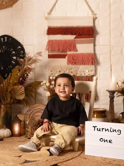Celebrating turning one with a sweet and simple portrait, this little boy sits next to a "Turning One" lightbox.