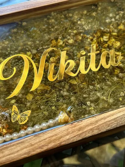 A close-up of the wooden nameplate, showing the detail of the preserved flowers and the elegant gold lettering of the name 'Nikita'.