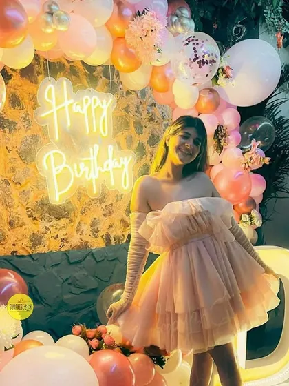 A dreamy birthday setup for an influencer, featuring a pastel pink balloon wall, a "Happy Birthday" neon sign, and a beautiful tulle dress that matches the decor's aesthetic perfectly.