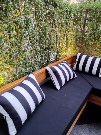 A detail shot of the comfortable cushions on the wooden bench, set against a living wall of green foliage that provides privacy and a natural backdrop.