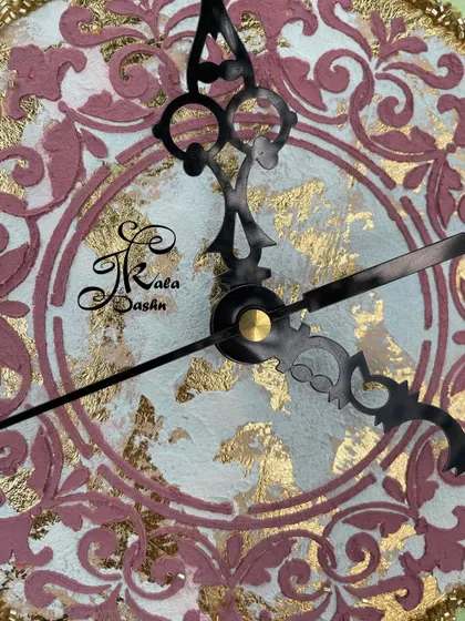 A macro shot of the clock's center, showing the intricate pink and gold leaf pattern on a white base. The ornate black hands complete the classic design.