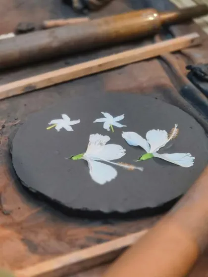 A student presses fresh flowers into a slab of dark clay, a beautiful technique for capturing natural textures. We encourage experimentation with different materials and methods.