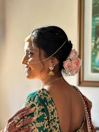 A classic low bun adorned with fresh pink roses and a delicate pearl nath-to-hair chain. This hairstyle is the epitome of grace and is perfect for a traditional wedding ceremony.