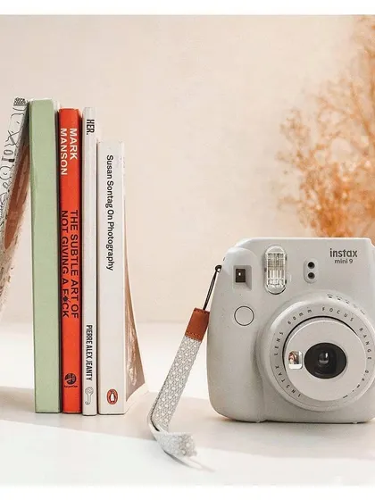 A white Instax camera is neatly arranged with a stack of books in a bright, minimalist flat lay. This style of product photography is popular for social media and e-commerce.