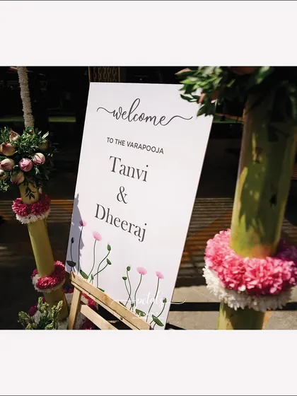 The welcome board for the Varapooja ceremony, adorned with charming illustrations and set against a backdrop of tuberose and nerium blooms.