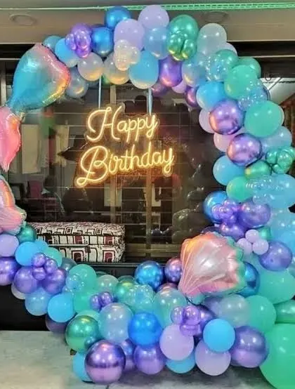 A magical mermaid-themed birthday decoration. This circular balloon arch uses shades of purple, blue, and teal, with mermaid tail and seashell foil balloons to complete the underwater look.