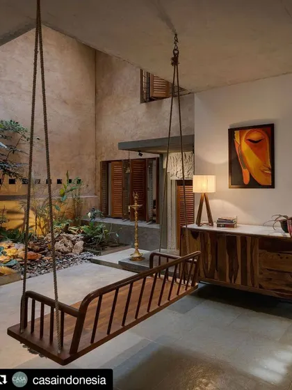 This view captures the essence of the home's indoor-outdoor connection. The wooden swing in the foreground looks out onto a lushly planted internal courtyard, creating a tranquil pocket of nature within the house.