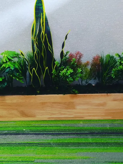 A wooden planter box filled with a mix of artificial plants and flowers. This type of arrangement is versatile and can be used on office floors, along walkways, or on reception counters.