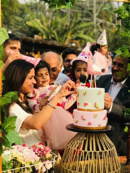 A heartwarming moment of a family celebrating a child's birthday, cutting the cake together surrounded by greenery.