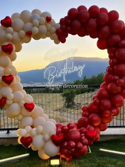 This outdoor heart-shaped balloon arch is perfect for a romantic birthday or anniversary. The red and white balloons and a 'Happy Birthday' neon sign create a stunning photo opportunity, especially at sunset.