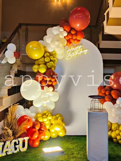 A modern and chic birthday setup for Nagu. The clean white arch is accented with a bold red, white, and yellow balloon garland, creating a stylish and contemporary look.