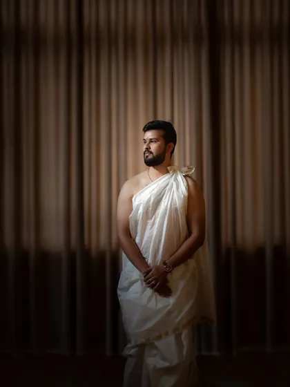 A classic portrait of the groom in traditional Brahmin wedding attire. The simple, elegant drapery and the soft, directional light create a powerful and dignified image.
