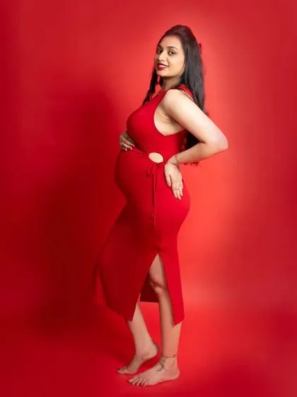 A confident and proud mom-to-be showing off her beautiful baby bump. The bold red dress and matching background make for a powerful and striking portrait.