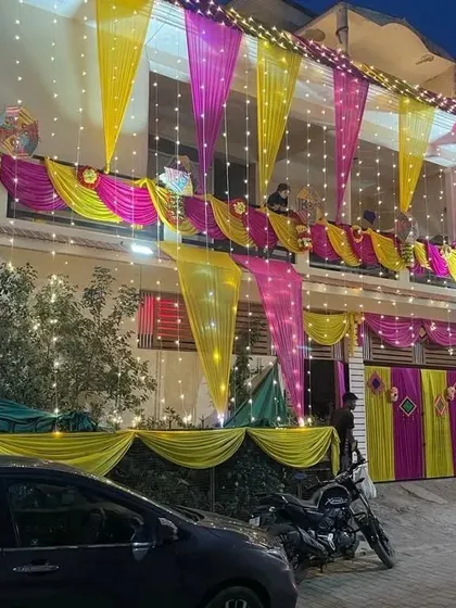A house decorated for a night function, with yellow and pink drapes on the balcony and gate, all lit up with fairy lights.