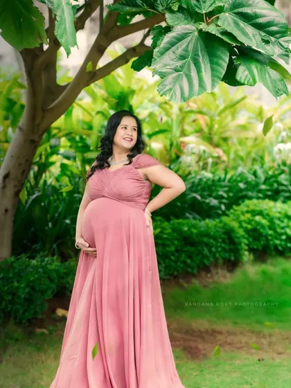 A solo portrait of a pregnant mother in a flowing pink gown, standing in a beautiful garden. The image captures a moment of peaceful reflection and joy.