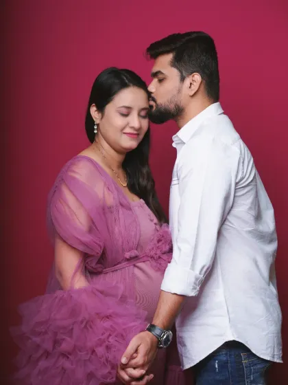 A tender moment between partners during a studio maternity session. The father-to-be gently kisses his partner's forehead, creating a feeling of love and protection.