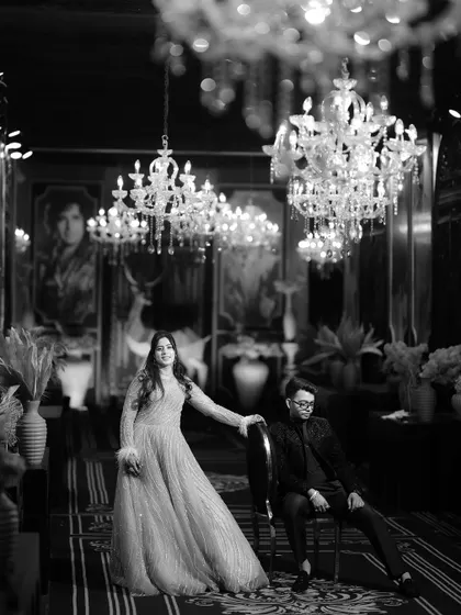 A stunning black and white photograph of the couple in a lavishly decorated hall. The grand chandeliers and their elegant poses create a timeless image of opulence and romance.