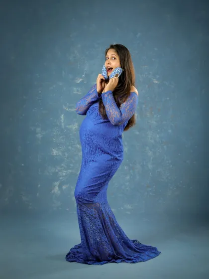 A fun and expressive portrait of a mom-to-be in a blue lace gown. Holding tiny baby shoes, her joyful expression is absolutely contagious.