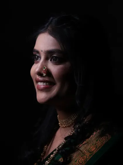 A dramatic, artistic shot of the bride. The lighting creates a beautiful contrast, highlighting her smile and the intricate details of her nath.