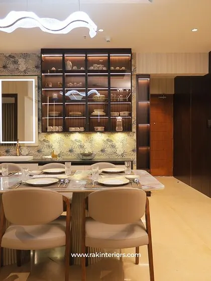 A sophisticated dining room with a marble-top table and beige upholstered chairs. The built-in crockery unit with a mirrored back and integrated lighting adds depth and luxury.