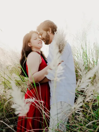 A romantic embrace surrounded by tall, feathery grass. The bright backlighting creates a beautiful halo effect, adding a dreamy quality to the image.