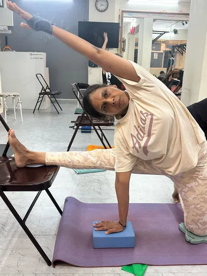 This student demonstrates a modified side stretch using a chair and block, showcasing how we adapt the practice to suit individual needs and flexibility levels.