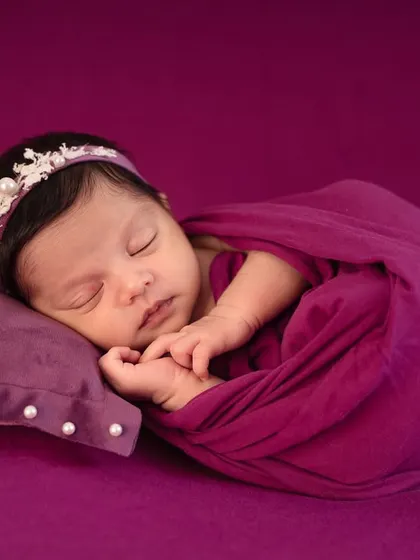 A close-up of a peacefully sleeping baby in a rich purple wrap, highlighting the delicate pearl headband and the serene expression.
