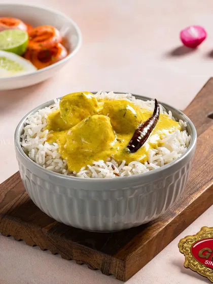 A bowl of Kadhi Pakora served over steamed rice, a classic comfort food from North India.