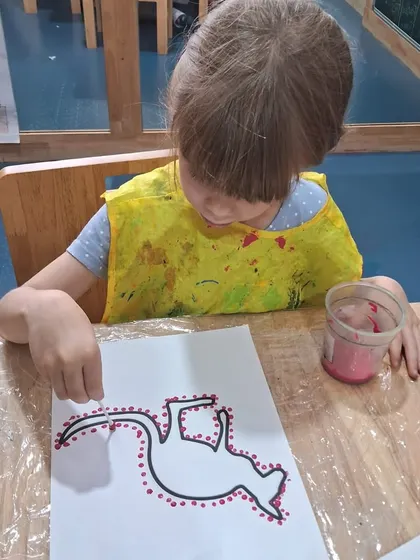 This girl is meticulously placing red dots around her drawing. Learning about global art forms like this broadens children's cultural awareness.