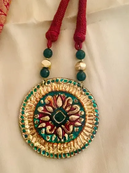 A close-up shot of the green and gold pendant, focusing on the central floral motif.