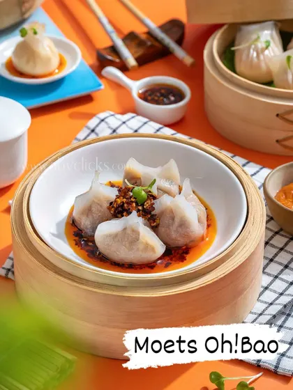 A vibrant shot of assorted dim sum served in a steamer with chili oil, against a bright orange background.