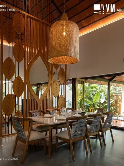 The grand dining space at Kuttiyil House, with its high, tiled roof, custom leaf-motif partition, and large woven light fixture, opens onto a veranda.