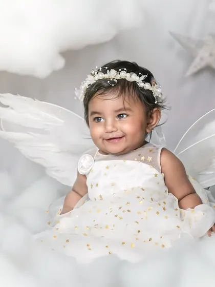 A baby girl dressed as an angel, smiling among the clouds and stars. A magical and heartwarming milestone photo.