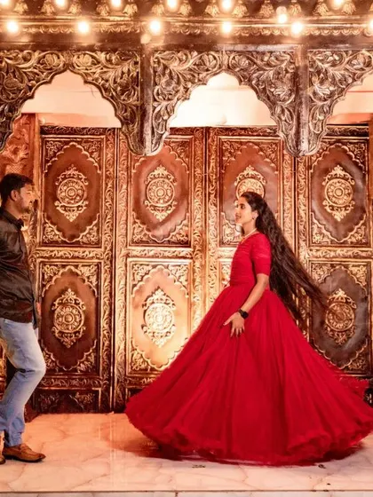 A dynamic shot of a bride in a swirling red dress facing her casually dressed groom against an ornate, warmly lit backdrop. It tells a story of modern love meeting timeless romance.