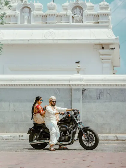 The groom, looking cool and confident in sunglasses, poses with his ride to the wedding, a classic motorcycle.