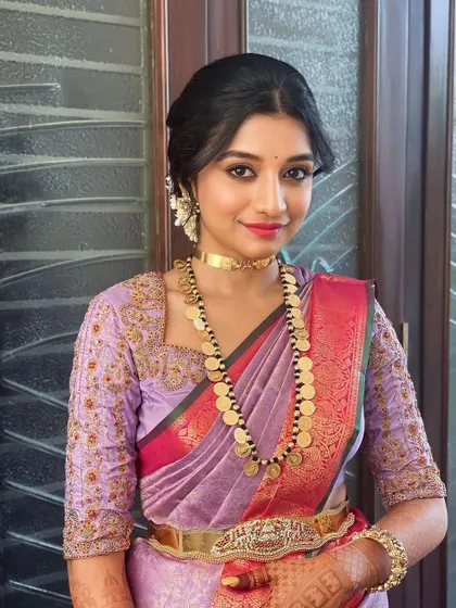 This client is wearing a beautiful lavender saree with a kasu mala. The makeup is soft and pretty, with a focus on rosy tones to complement the outfit.